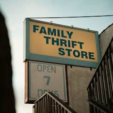 Retro-style sign for a family thrift store with stairs and wooden railing in view.